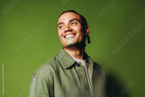 Smiling man in the studio wears artistic face paint with casual fashion