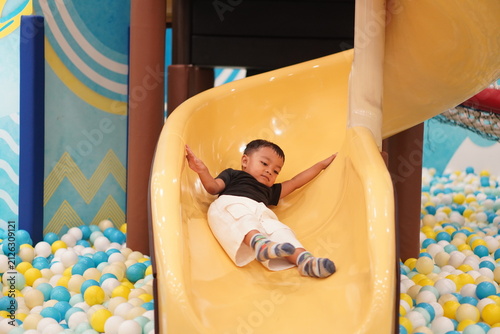 Asian Toddler Boy Gliding Down Yellow Slide into Ball Pit
