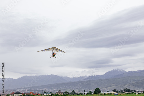 Fotografía Motorized hang glider ultralight trike flying isolated in gray overcast sky background
