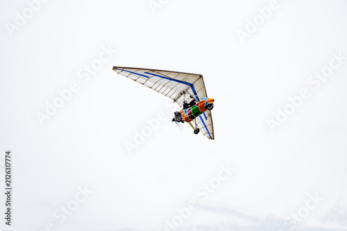 Cuadro en lienzo Motorized hang glider ultralight trike flying isolated in gray overcast sky background