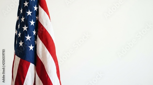 A vertically hanging american flag positioned on the left side with a clean white background and copy space