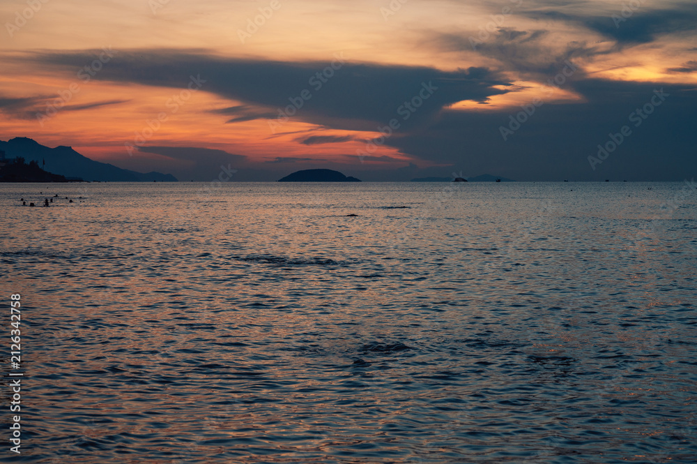 Fototapeta premium Crowds of people enjoying a warm morning swim in the ocean during a colorful sunset, creating a relaxing summer beach atmosphere, Nha Trang, Vietnam
