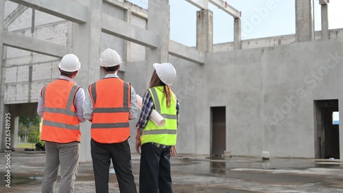Construction engineers review a blueprint and discuss project plans at a building site. Concept of civil engineering, teamwork, architecture, construction management, and development.