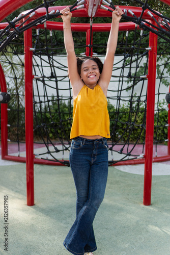 Teen girl smiling, happily hanging on playground structure