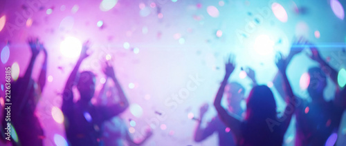 Party crowd dancing at nightclub in blurred motion with hands raised, illuminated by glowing neon lights, lens flares, and falling confetti bokeh, ideal for music festival banners