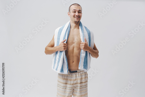 Smiling Shirtless Young Man Holding Beach Towel on Grey Background