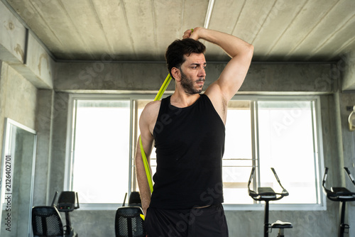 Adult Caucasian man stretching shoulder with green resistance band in modern gym, mobility warm up before strength workout, active male athlete fitness lifestyle for personal training and wellness ads