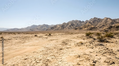 Arid desert landscape with cracked earth and distant mountains under a clear blue sky