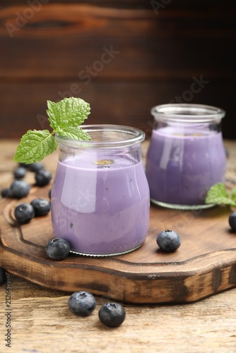 Foto Tasty blueberry smoothie in jars, fresh berries and mint on wooden table, closeu