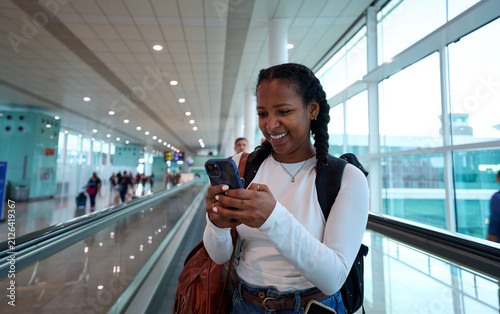 Smiling woman checking phone on moving walkway inside airport terminal on the way to vacations. Copy space.