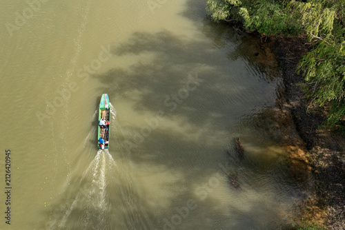 фотографія Aerial view of a small boat with people navigating the Tamis river, passing by a lush riverbank with trees in Pancevo, Vojvodina, Serbia