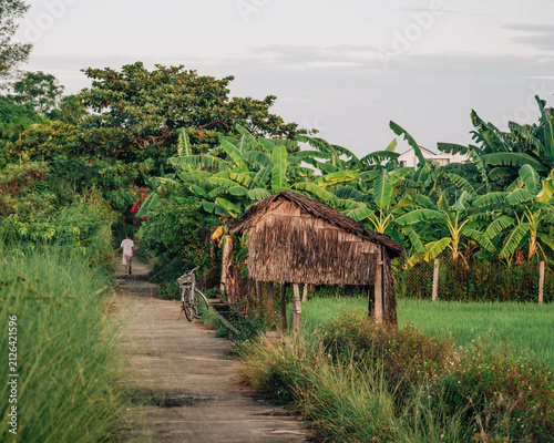 Fotografía Traveler Walking Along Country Path Next to Thatched Hut
