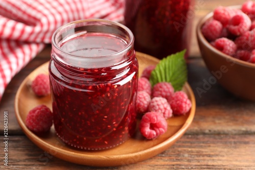 Tasty raspberry jam in jars and fresh berries on wooden table, closeup