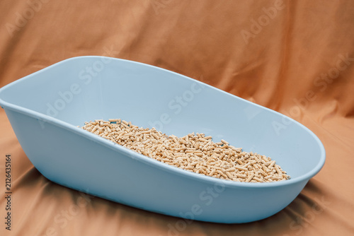 Wood pellets are held in  hand above a larger pile of wood pellets in  storage area.  blue plastic litter box sits on a brown surface filled with wood pellets.  care for  pet, ready for use indoors