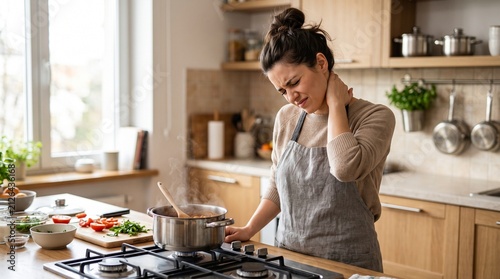 Kitchen Distress: A woman in an apron clutches her neck in pain while cooking in a well-lit kitchen, conveying discomfort and the struggle of daily chores.