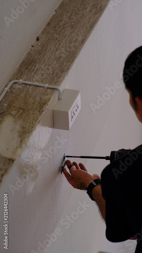 The builder with hammer drill perforator equipment making hole in wall at construction site.