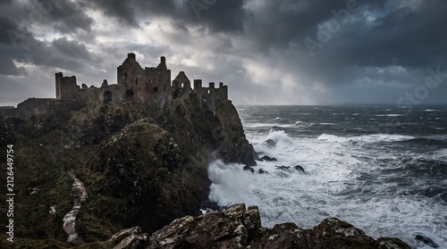 Ancient castle ruins perched on a dramatic cliffside overlooking a stormy sea with crashing waves evoking a sense of history and wild nature