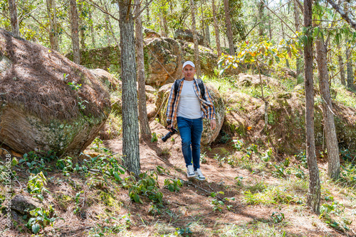 Quadro su tela Man with backpack and camera hiking through a vibrant green forest, navigating a