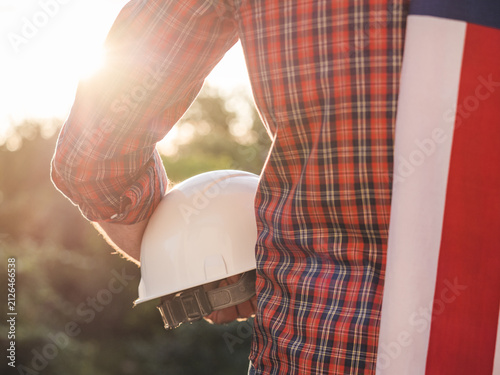 Cuadro en lienzo Construction worker holds a white hard hat with an American flag draped over his shoulder