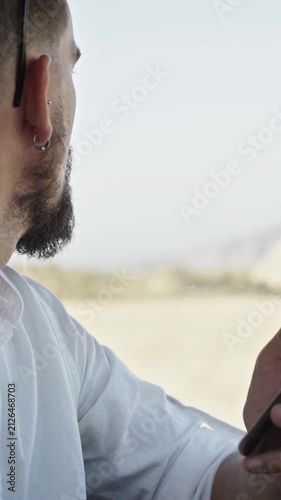Caucasian man using cellphone inside car in a desert, sending text messages. Concept of people connected everywhere. Copy space vertical footage.