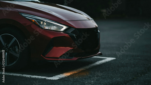Red car parked in a parking lot. Modern vehicle front view at night.