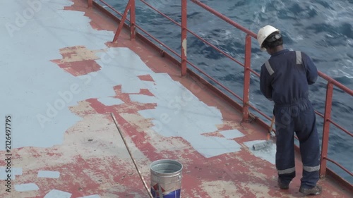 manual applying of protective deck coating on a cargo ship while underway at sea