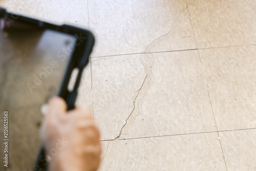 Photography A man at work, an inspector taking a picture of the cracked garage floor of a re