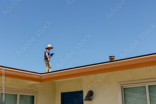 House during day with Single Family Home and home inspector blue uniform walking on roof shingles