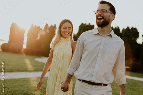 Фотография Couple walks hand in hand during sunset in a park with green grass and trees