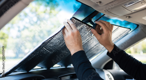 Driver installing reflective sun visor on car windshield to block heat