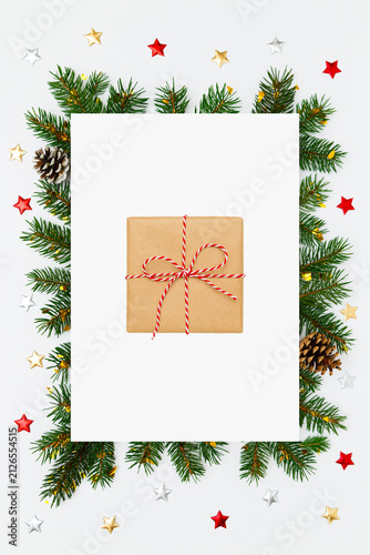 Christmas, New Year vertical holiday layout. Christmas gift in craft paper in frame of fir tree branches and decorations on white flat lay background. Perfect for holiday greetings, banners, social