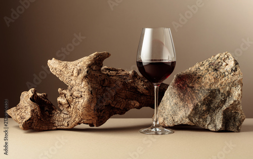 Foto Glass of red wine with old driftwood and a piece of granite rock on a beige background