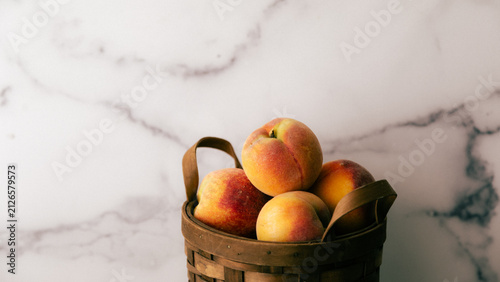 Fresh peaches collected in a basket placed on a marble surface during afternoon light background