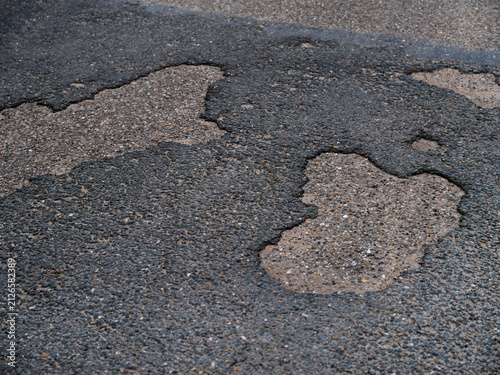 Fotografía Large potholes and cracks in a worn asphalt road surface reveal the gravel beneath
