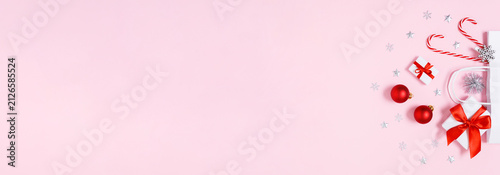 Minimal Christmas banner with white paper gift bag, presents, baubles and candy canes on soft pink copy space for holiday sales, social media ads and festive designs, flat lay.