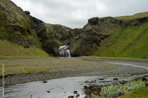 Konstfotografi Scenic Icelandic landscape with Stjornarfoss cascade waterfall, mountain river and mossy hills under overcast sky