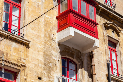 Fotografía Vivid red wooden gallarija balcony contrasts with weathered limestone facade and