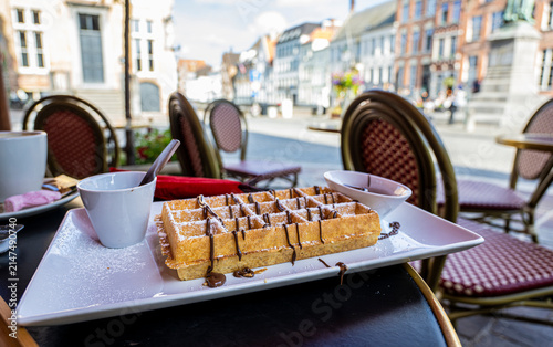 Traditional Belgian waffle with chocolate topping served on a café terrace in Bruges featuring historic European architecture and soft blurred city background