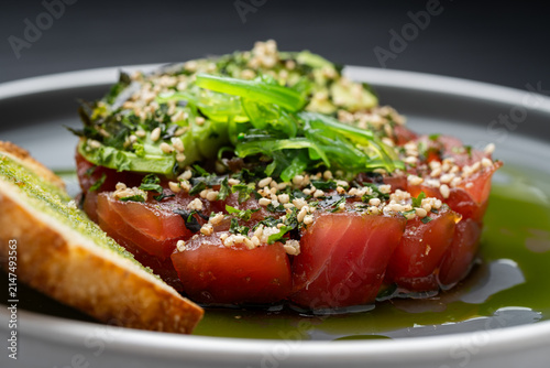 Herbed fish with veggies. A plate shows diced fish topped with herbs and vegetables, garnished with sesame seeds, served on a light sauce.