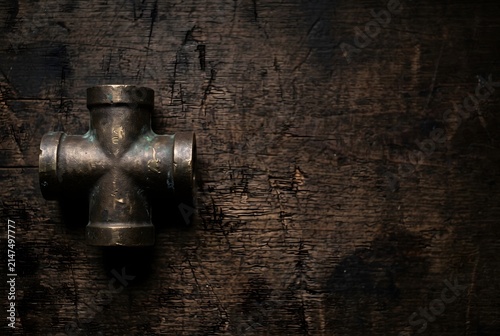 Vintage heavy brass industrial cross pipe fitting on dark wooden workbench with copy space