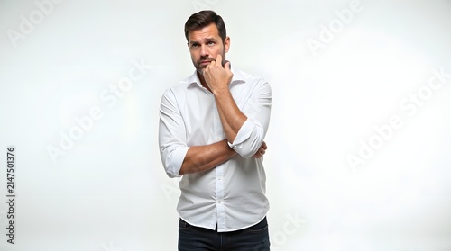 Pensive Caucasian male in a white shirt looking contemplative against a light background.