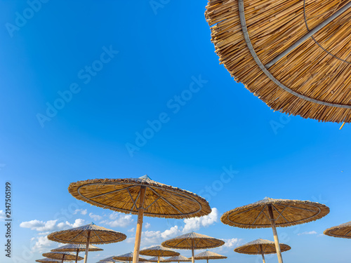 Umbrellas stand on the beach under the blue sky with clouds in the distance, showing a sunny day at a coastal location