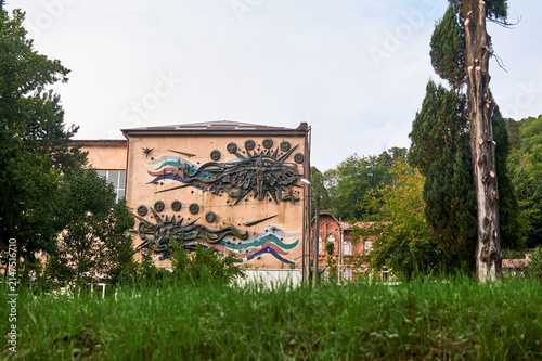 Obraz na płótnie Beige building facade with an abstract metal bas-relief and colorful wavy lines (sun, waves, stylized figures)