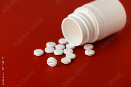 Принти на полотні In a close-up view, a white bottle tips over, releasing smooth, round tablets onto a bold red background