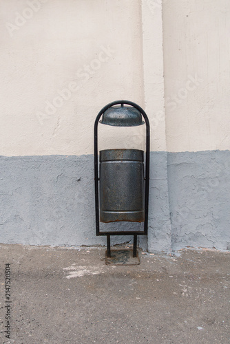 Black wall-mounted trash bin hangs on a building exterior, urban waste receptacle