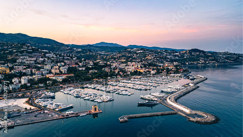 Aerial view of Sanremo port and coastline at twilight with sunset sky harbor lights reflecting on sea water and city stretching along the Ligurian coast Italy