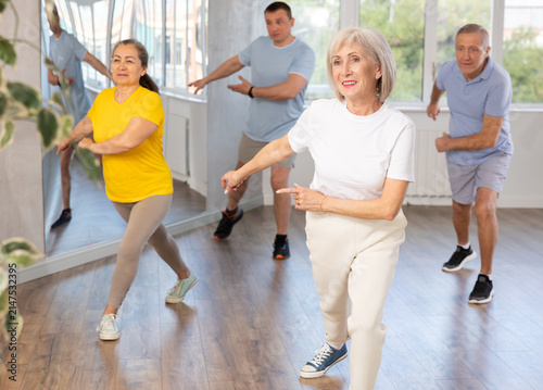 Obraz na płótnie Expressive cheerful woman participating in upbeat Zumba class for group of seniors in mirrored fitness studio