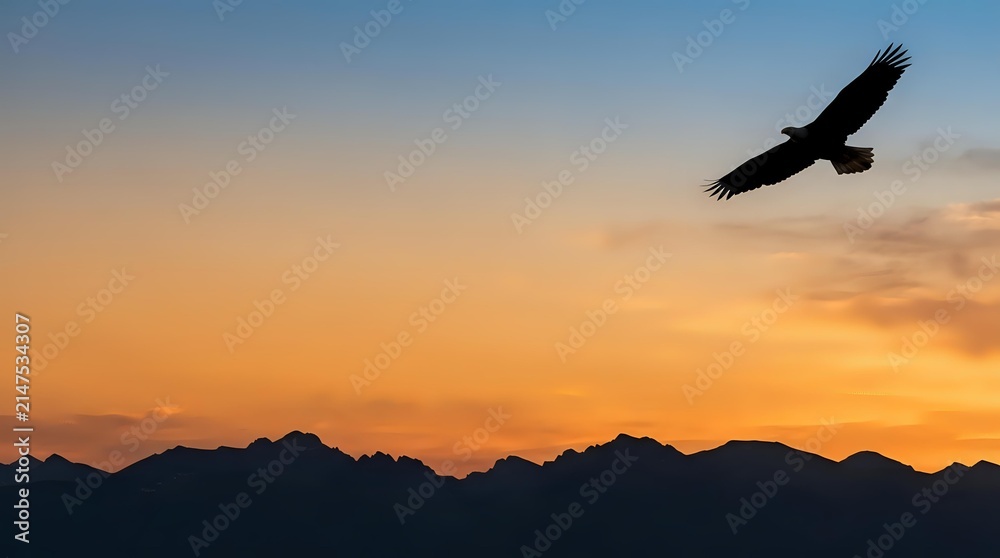 Naklejka premium Silhouette of a large bird of prey soaring against a dramatic golden and orange sunset sky with mountain ridges below, conveying freedom and nature.