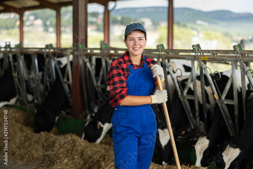 Girl is employee of company during break in work. She stands next to animal pen, with rural hilly landscape in background.
