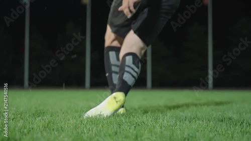 A footballer's feet kick a ball on the pitch at night. Filmed in slow motion